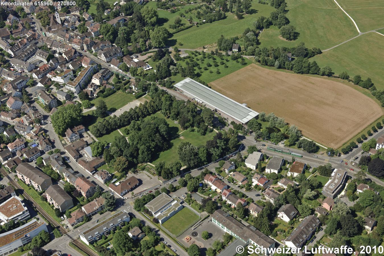 Fondation Beyeler in Riehen (BS). Norden gegen den rechten untern Bildrand. Museumsbau des italienischen Stararchitekten Renzo Piano. Vorgelagert der Sarasin-Park. Links oben der Dorfkern von Riehen. Abgeerntetes Feld: 'auf dem Mühlebrühl'.